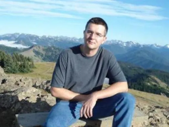 Milos Babic sitting on rock with mountains in background