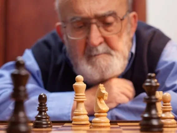 Elderly man staring at chess board pieces