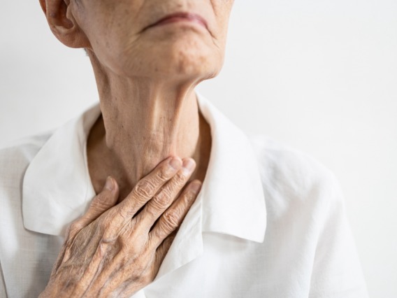 Elderly individual touching throat with fingers
