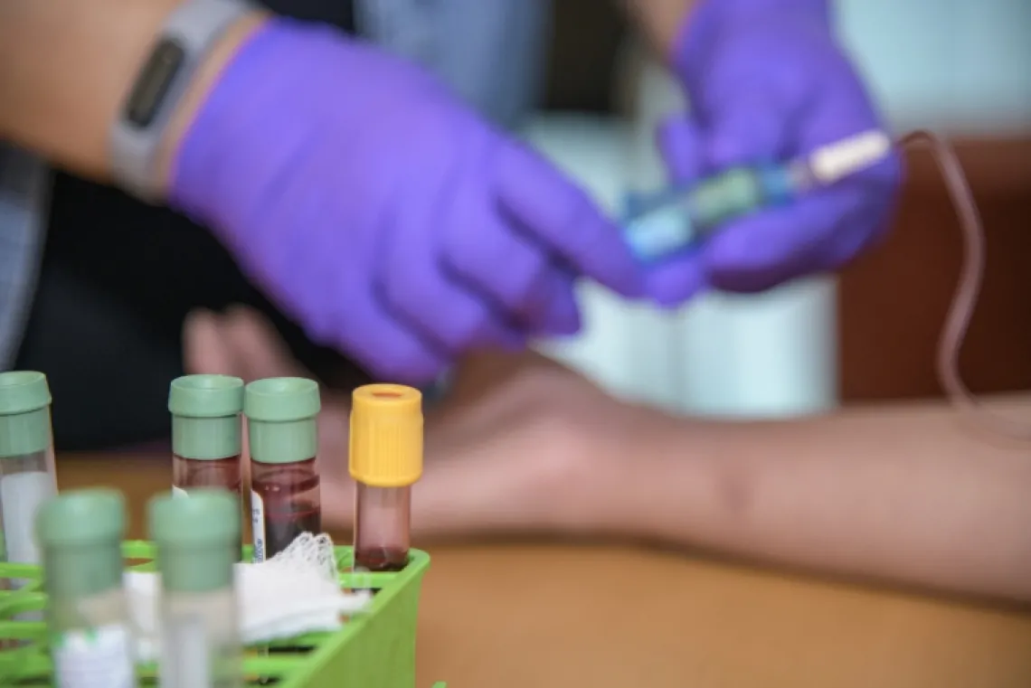 Close up of viles of blood, phlebotomist drawing blood in background