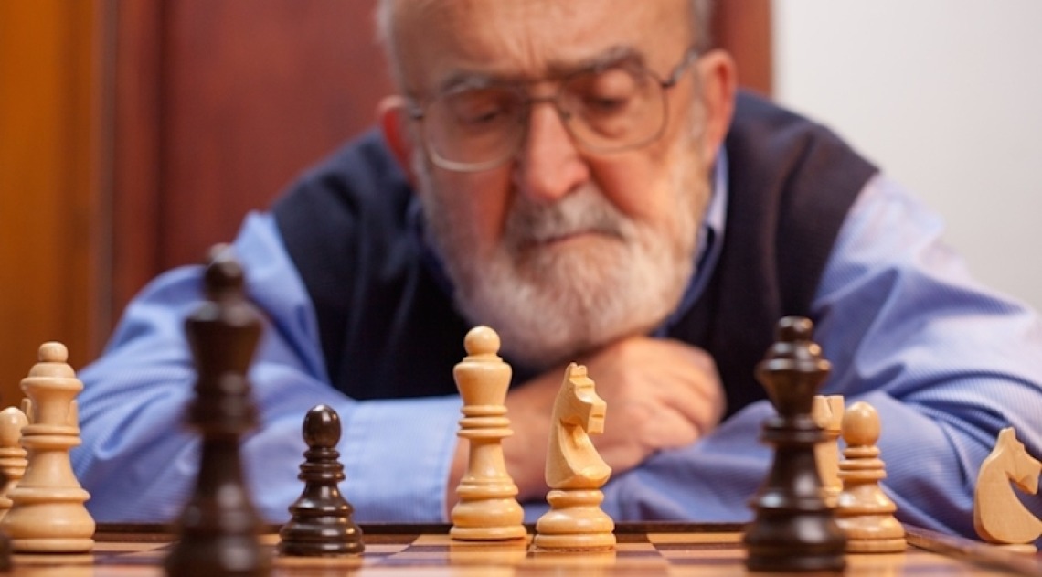 Elderly man staring at chess board pieces