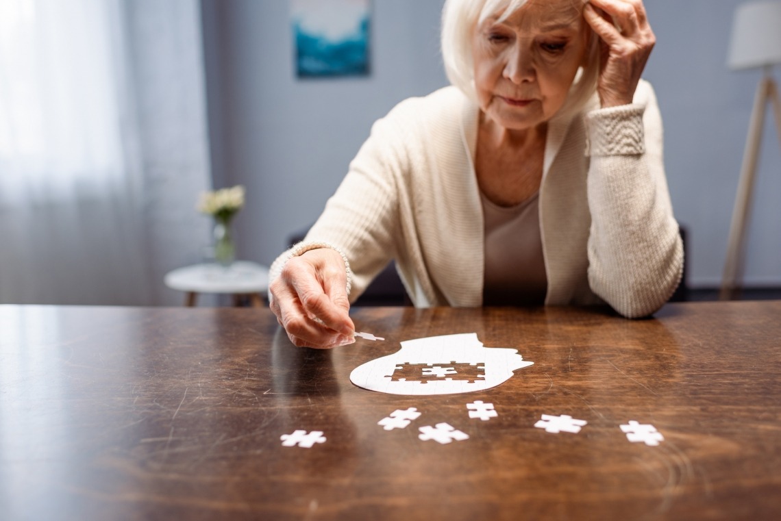Elderly woman struggling with putting pieces of a puzzle together in the shape of a human head