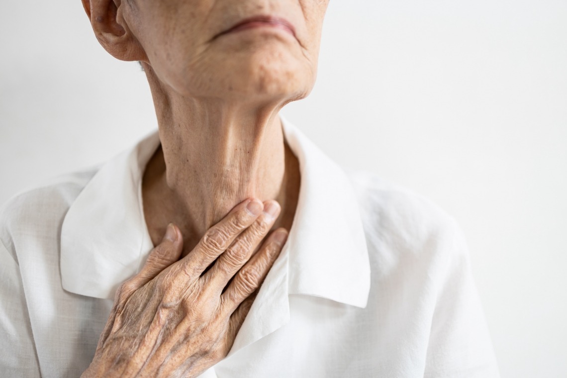 Elderly individual touching throat with fingers