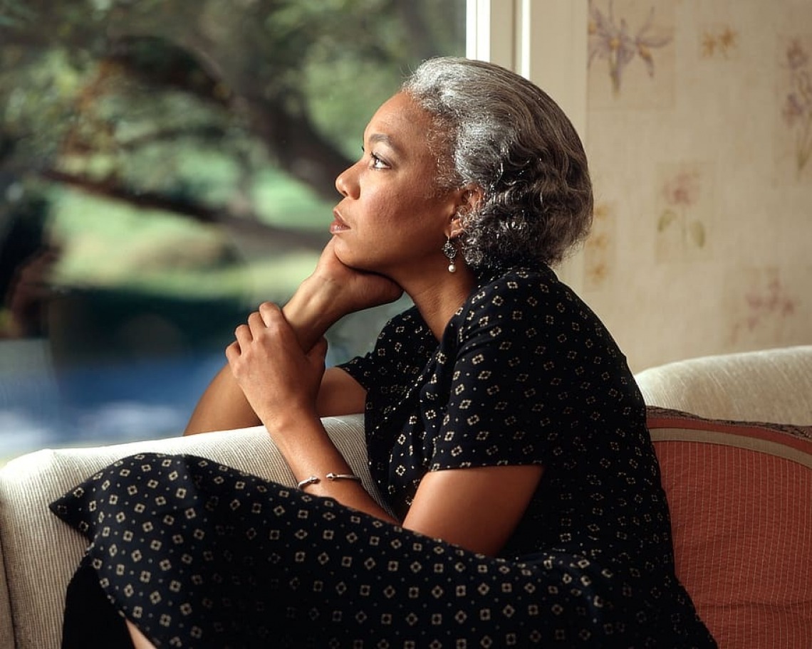 Woman sitting on couch, staring out the window pensively