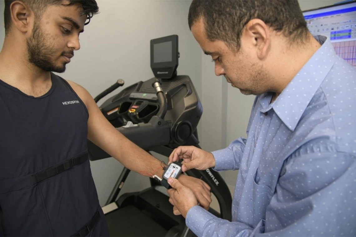 Man placing research device on patient's wrist, treadmill in background